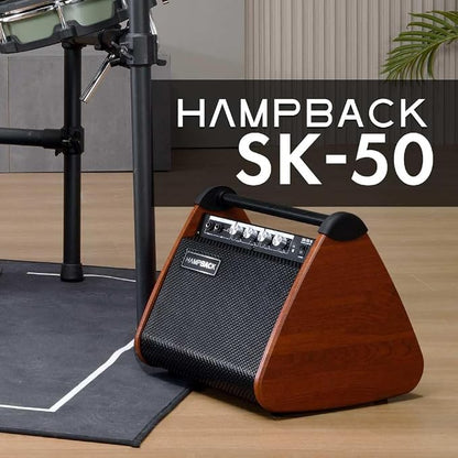 A HAMPBACK SK-50 portable speaker with a brown wood-grain finish and black mesh grille, shown on a wooden floor next to a drum kit stand. A dark overlay with white text reads 'HAMPBACK SK-50'.